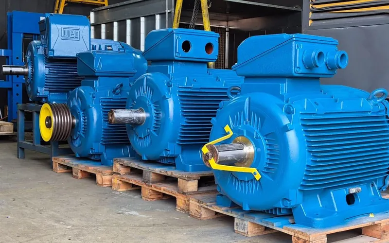 Motores elétricos de corrente alternada de grande porte, recuperados e pintados, sobre paletes na oficina da Techservice