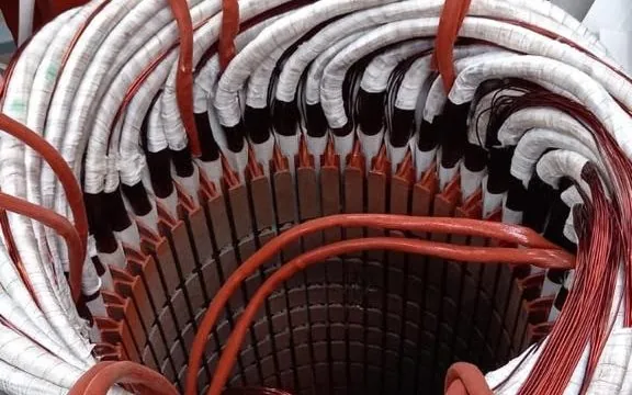Interior de um estator com as bobinas de fio de cobre já inseridas nas ranhuras e a isolação branca aparente, durante o rebobinamento na oficina da Techservice